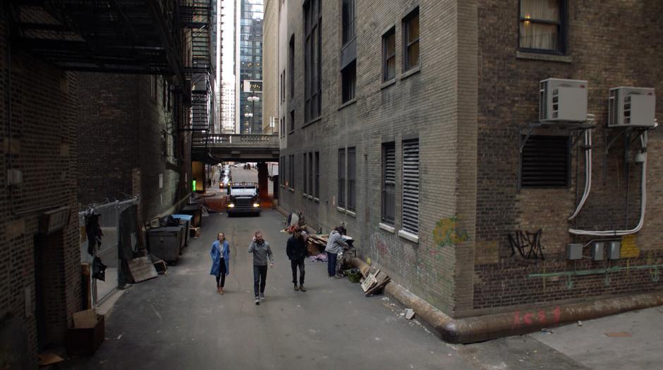 Kara, Oliver, and Barry walk down the alley as an armored car drives up behind them.