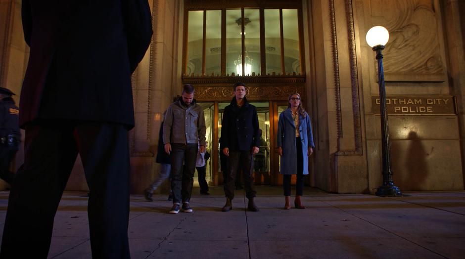 Oliver, Barry, and Kara stand in front of the station while the man in the suit encourages them to come with him.