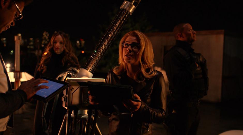 Felicity tries to explain the device to Diggle while working on the device with Curtis and Caitlin.