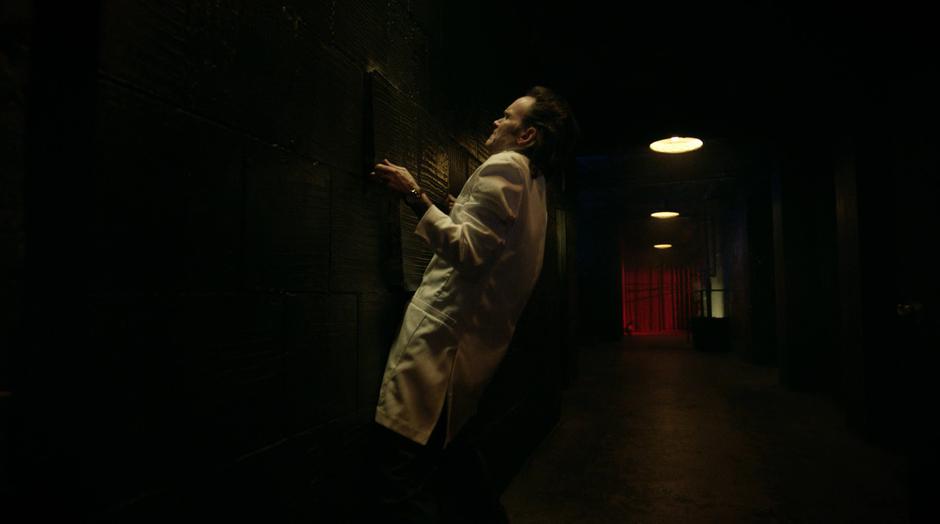 Dr. Deegan lifts a panel off the wall to access his secret stash.