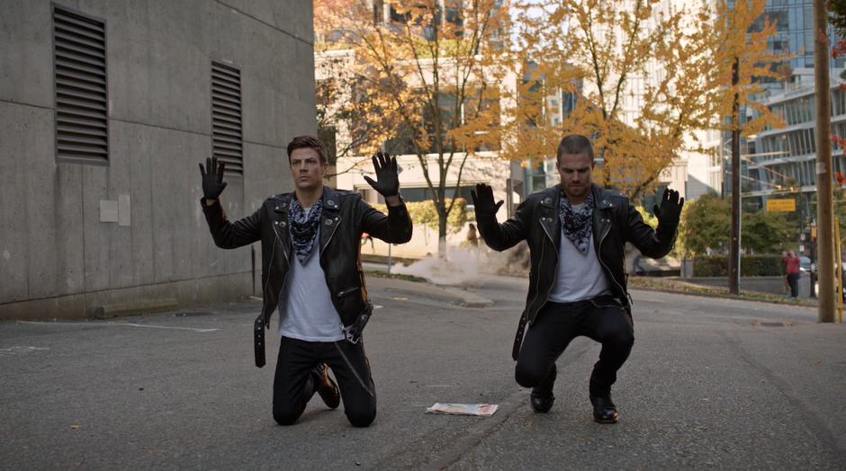 Barry and Oliver put their hands in the air while kneeling down on the ground.