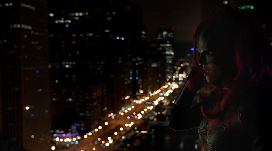 Kate Kane talks to Oliver on the coms while standing on the rooftop.