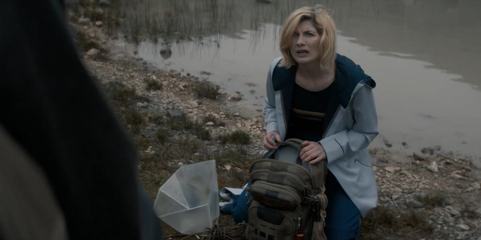 The Doctor kneels down over her backpack with the strange device.