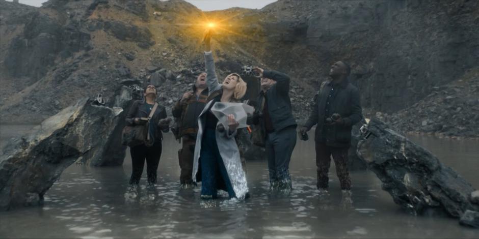 The Doctor uses her sonic to activate the entrance to the shrine while standing the water with Yaz, Paltraki, Graham, and Ryan.