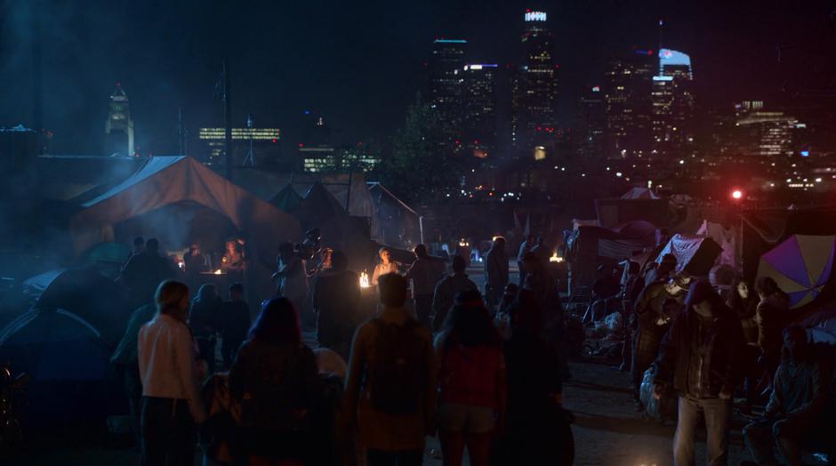 The kids walk through the camp while downtown looms in the background.