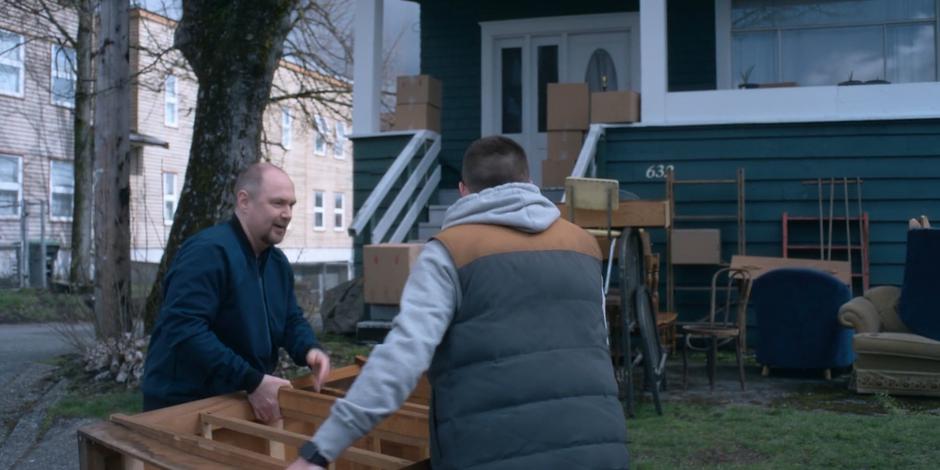 Gary and Trevor carry a dresser to the lawn in front of the house.