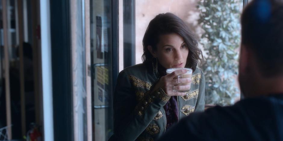 Kat takes a drink of her coffee while sitting at the front window with David.