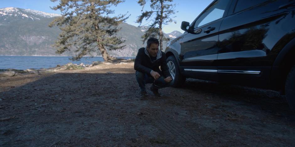 Grant kneels down next to his car to examine hte old tire tracks.