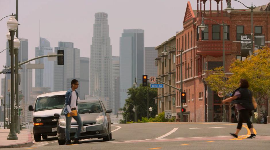 Alex crosses the street with downtown visible in the distant background.