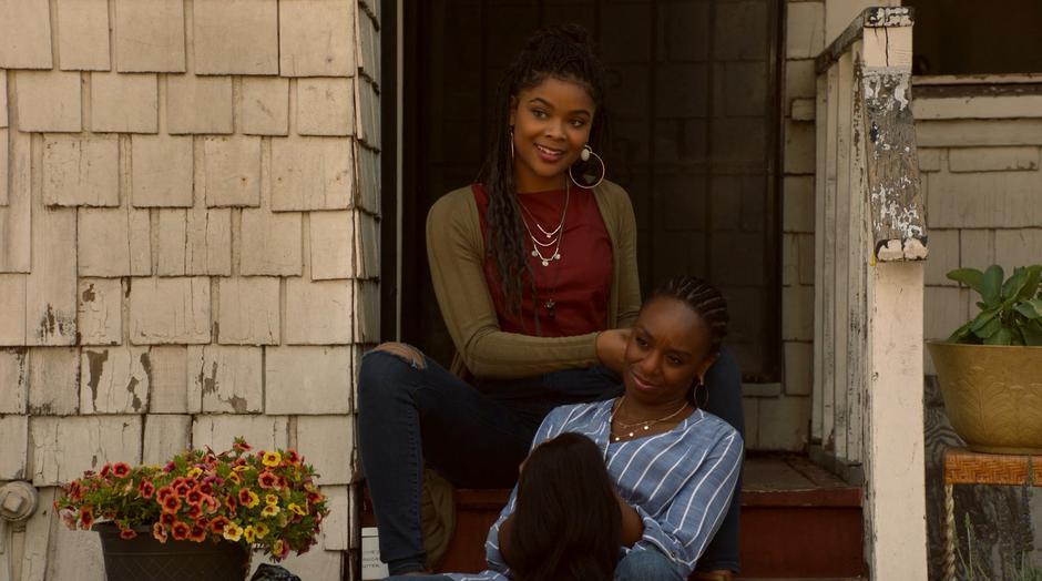 Livvie smiles up at Alex while working on Tamar's hair on the back steps.
