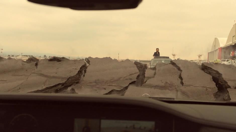 A wall raises up from the ground in front of Geoffrey as Nico rides away in the car while standing through the sunroof.