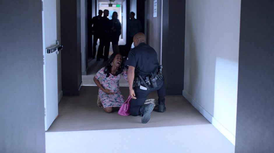 Tamar kneels in the hallway crying out after learning about Darius' fate while a police officer kneels with her.