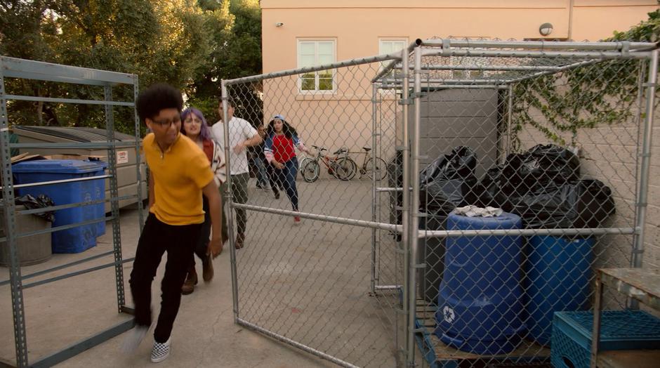 Alex, Gert, Chase, Molly, and the others run past the dumpsters to get a good look at the school over the wall.