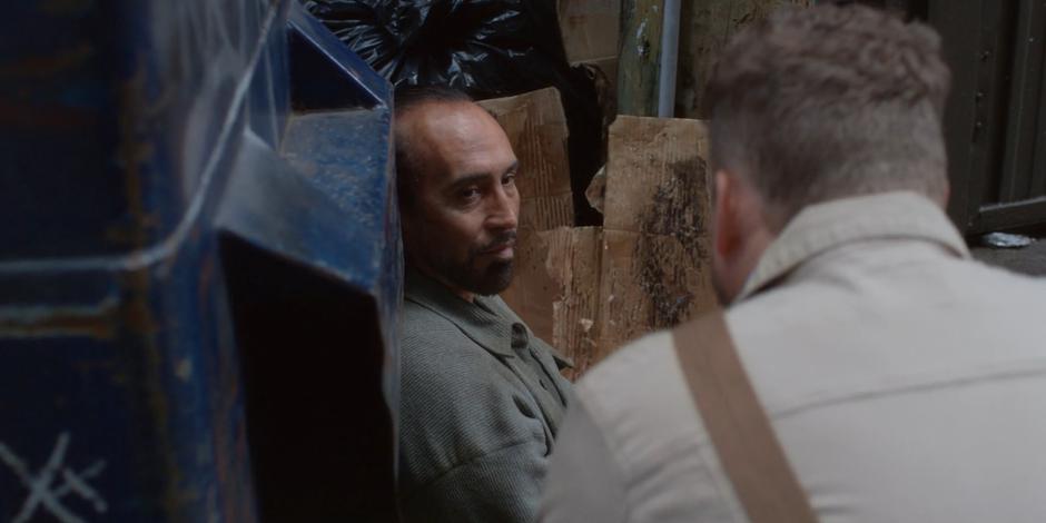 David kneels down and talks to one of his clients who is sitting against the dumpster.