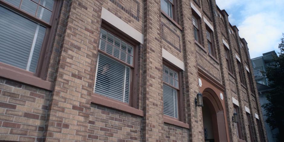 Carly stands at the window of the apartment and looks out at the street.