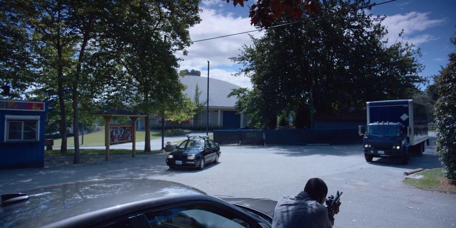 Jeff takes cover behind his car as a sedan and a truck pull up to the building.