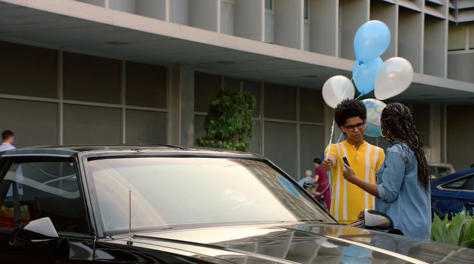 Alex holds the balloons out to Livvie as she is filming the new baby.