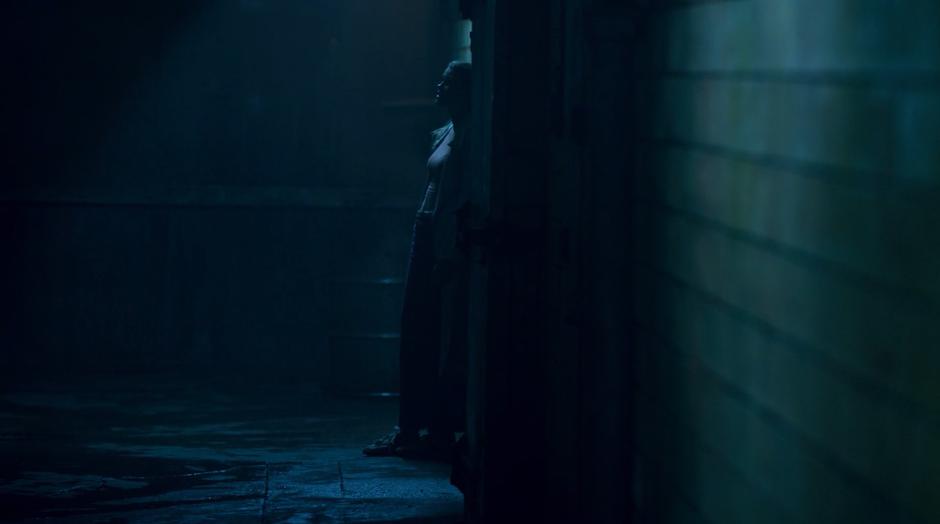 Karolina leans against the wall on the inside of the darkened warehouse.
