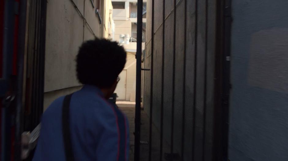 Alex runs through a gate and down a narrow alley.