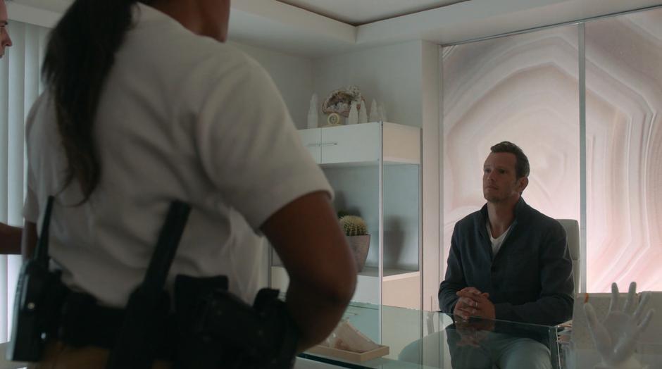 Frank sits at the desk while two guards escort Leslie in to talk with him.