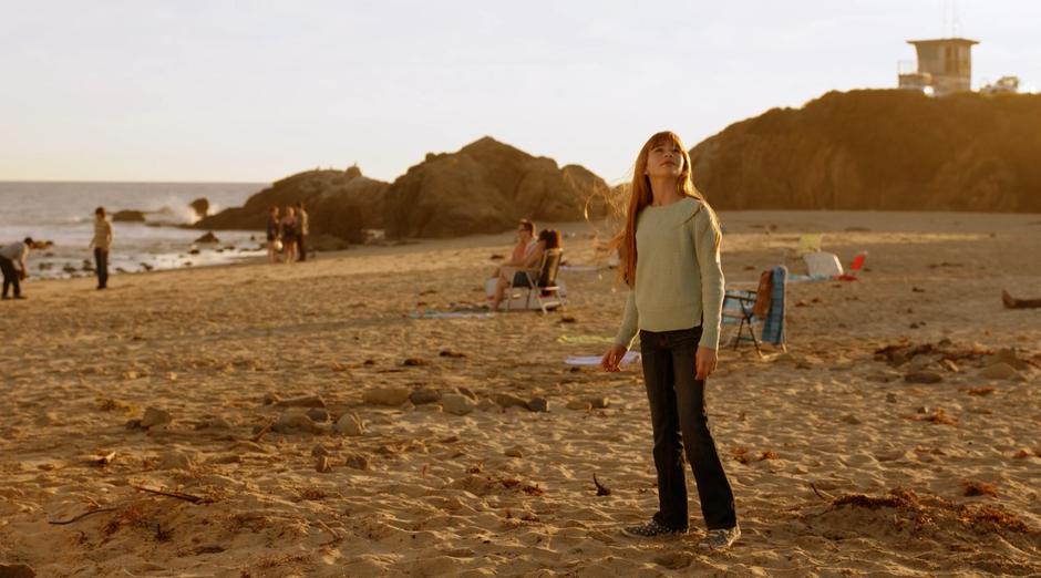 Kara stands on the beach staring up at the sky.