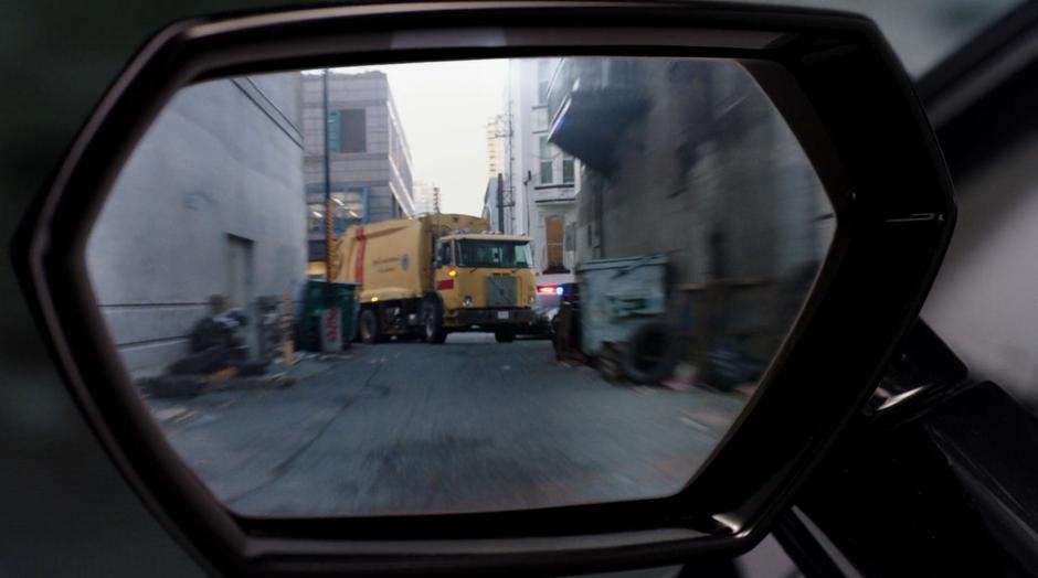 The garbage truck is visible in the side mirror blocking the end of the alley.