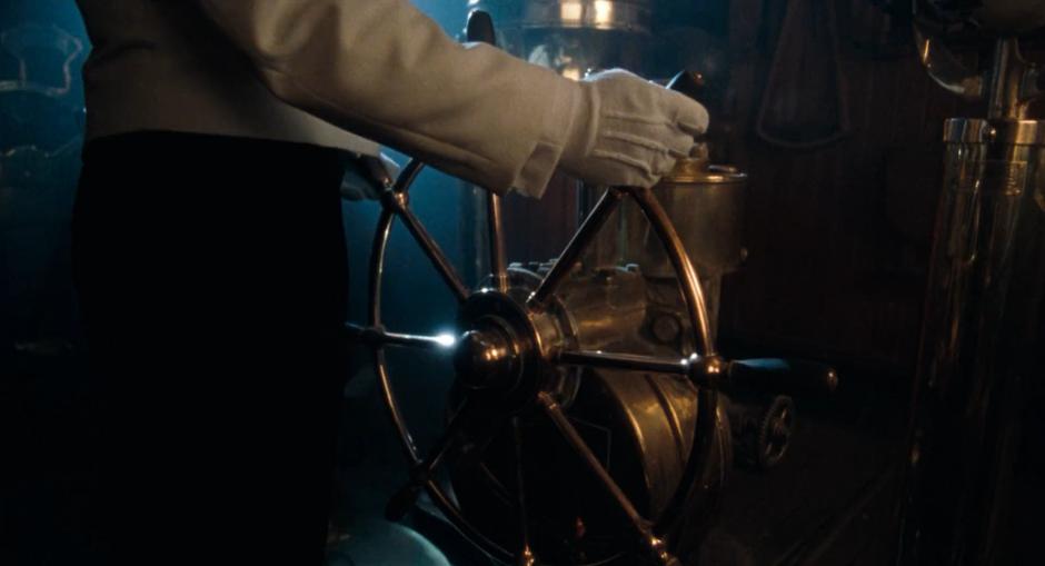 One of the ship's crew steers the vessel using a brass wheel.