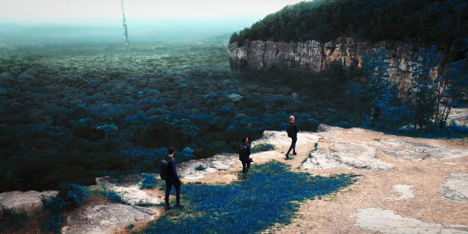 Ash, Michael, and Saru walk along the top of a ridge while the beacon emerges from the forest in the distance.