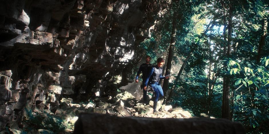 Ash and Michael climb over some rocks beneath a cliff face.