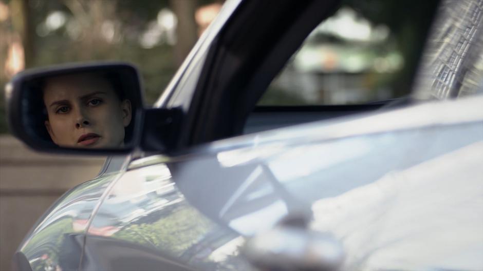 Kady watches Mark in the side mirror of her car.