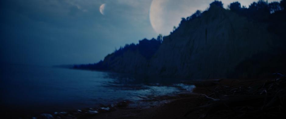 Two moons hover of the cliffs above the water.