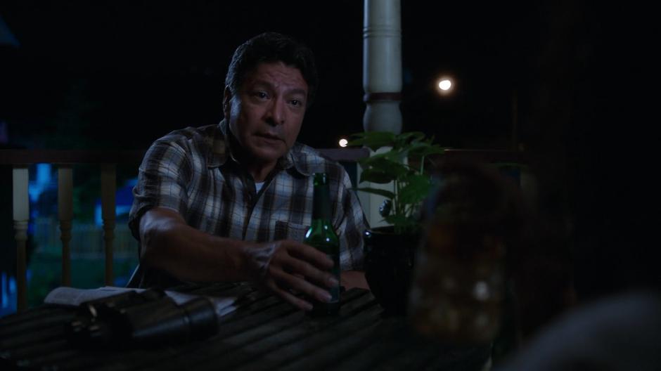 Dale grabs his beer from the table while talking to Susan on the back porch at night.