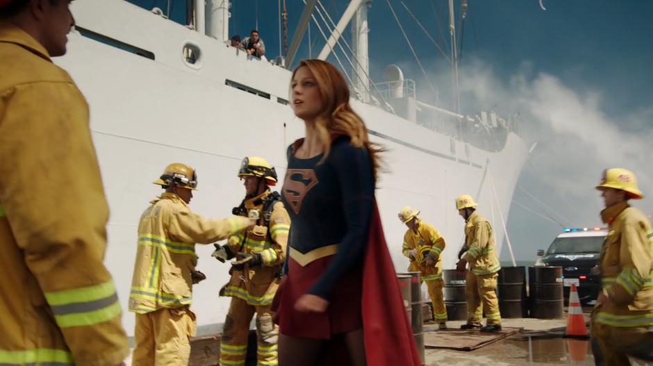 Kara lands on the dock and talks to two firefighters.