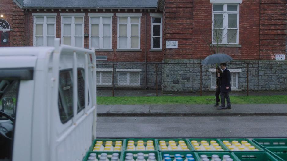 Mel and Harry walk down the street under an umbrella.