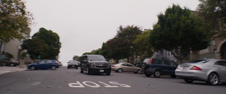Two black FBI SUVs drive down the road towards Scott's house.