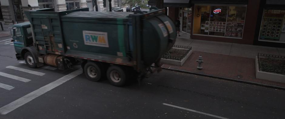 The garbage truck drives off down the street.