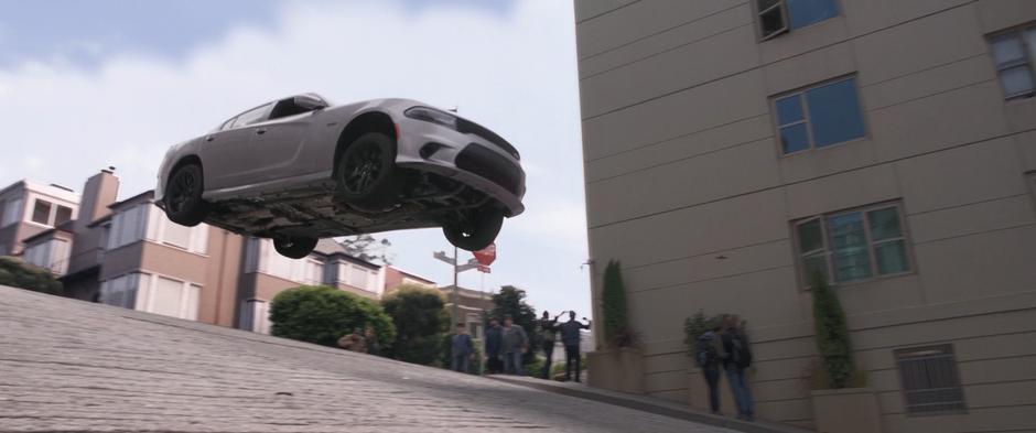 A purusing car flies into the air over the top of a hill.