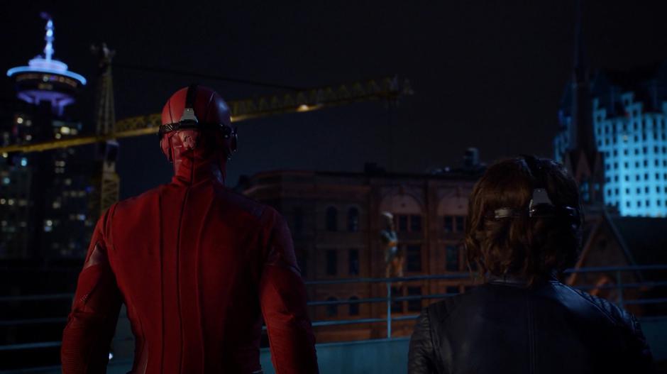 Barry and Nora look across the way as King Shark is hung from a crane by Grodd.