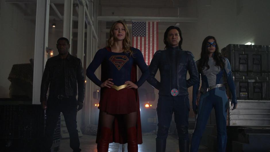 Kara stands with her hands on her hips in front of J'onn, Brainy, and Nia.