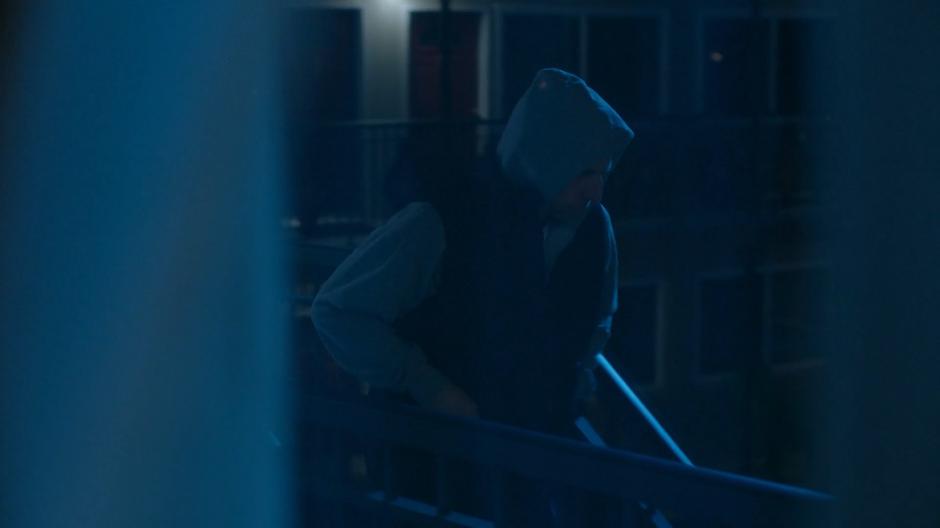 A man in a hoodie is visible walking down the stairs through the motel room window.