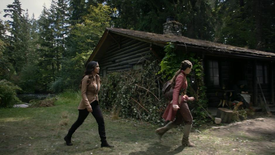 Margo and Fen walk around the side of the cabin to where a figure in a green cloak is sitting.