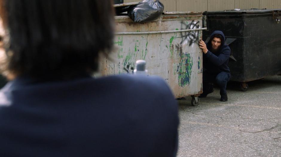 Konane comes out from behind a dumpster and sees Mona.