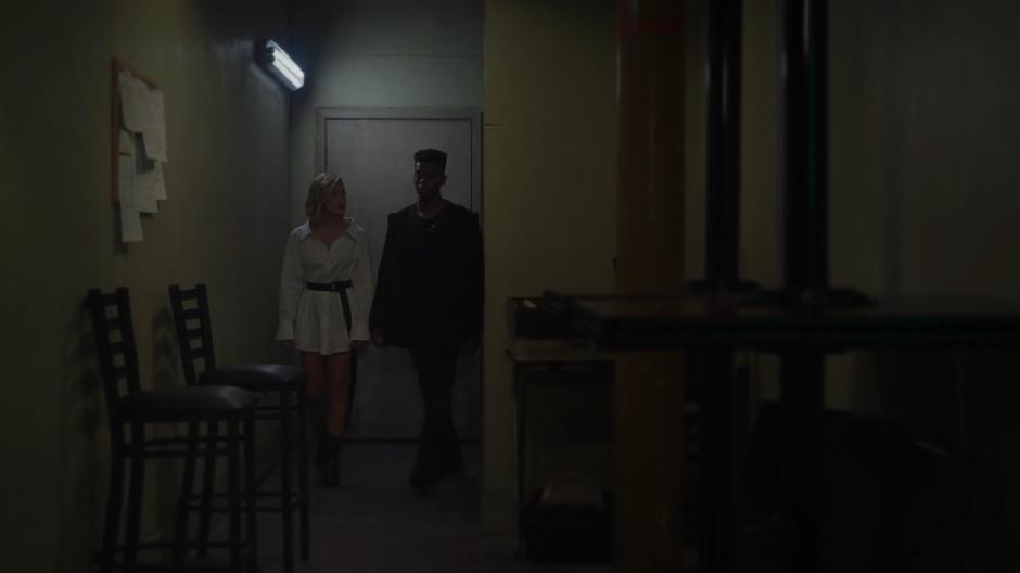 Tandy and Tyrone walk down the back hallway from the back room talking.