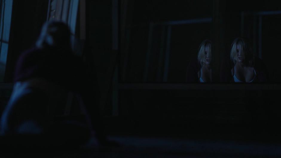Tandy kneels on the ground and stares at her reflection in the darkened room.