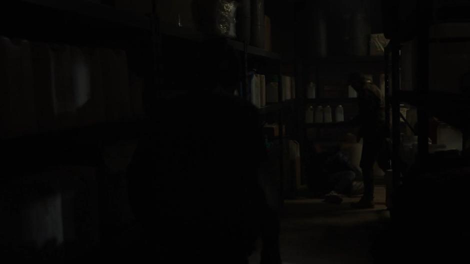 A gang member knocks Tyrone to the floor while another approaches through the storage room.