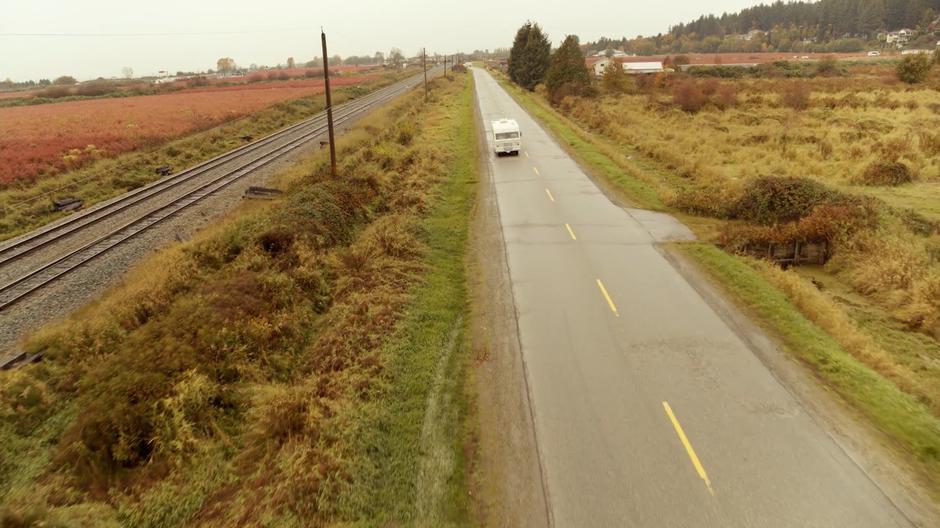 The RV drives down the highway next to a line of train tracks.