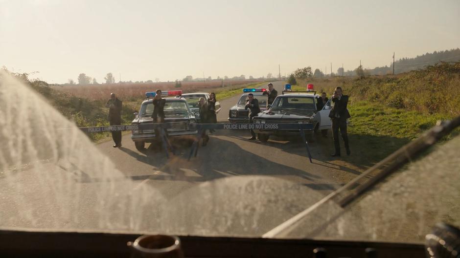 A while group of Time Bureau agents in purloined State Police cars hold their guns at the RV as it stops at their roadblock.