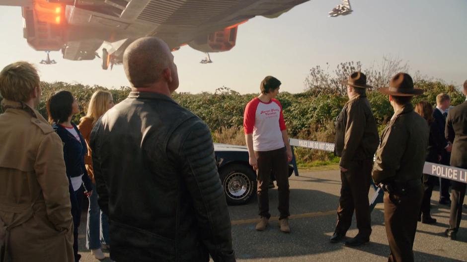 The Legends and the Time Bureau agents look behind themselves as the Waverider flies overhead.