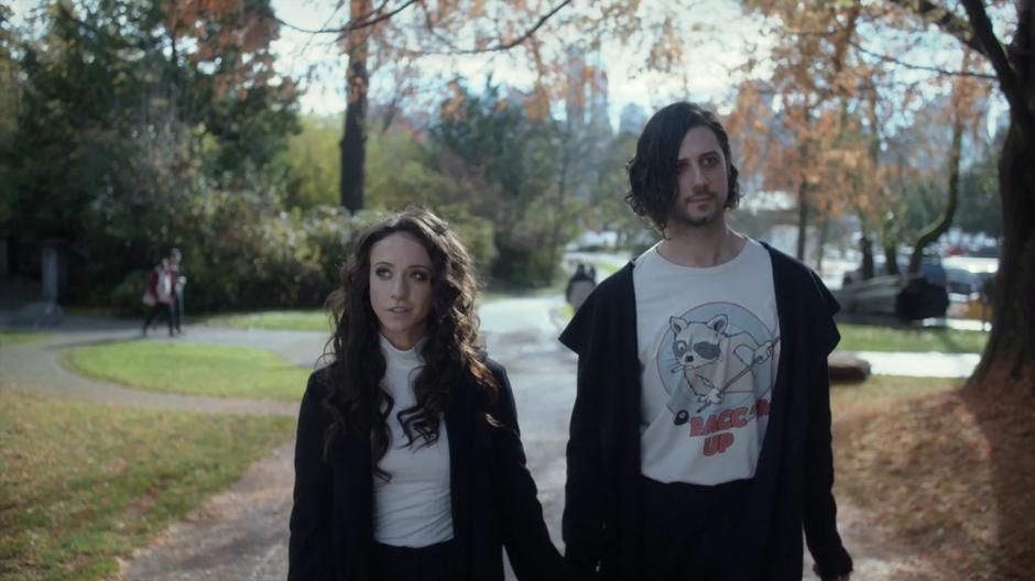 The sister and the monster walk down the path through the park holding hands and discussing their time apart.