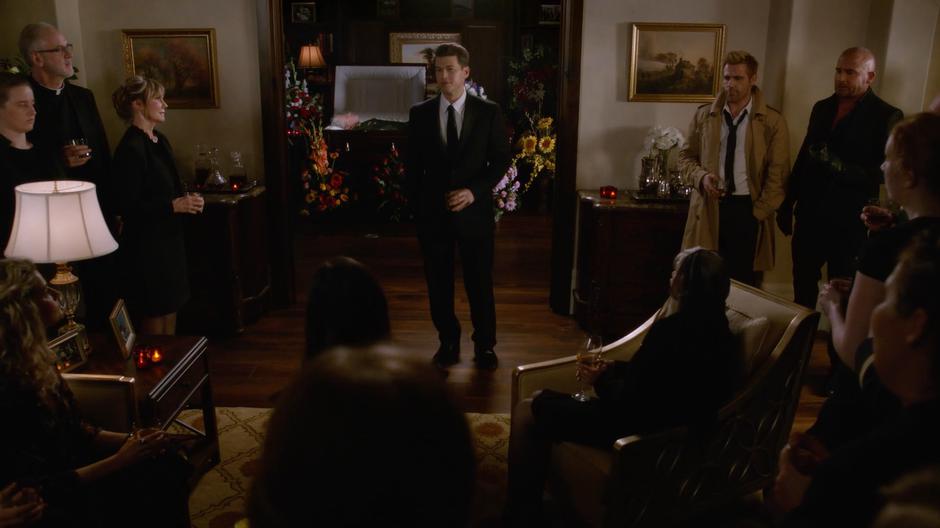 Dorothy Heywood, Constantine, Mick, and the other people at the memorial watch Nate as he starts to give his eulogy in front of his father's coffin.